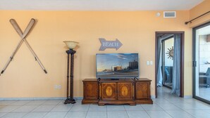 Een kamer met een houten kast, een televisie waarop een strand te zien is, en een bord aan de muur dat de richting naar het strand aangeeft.