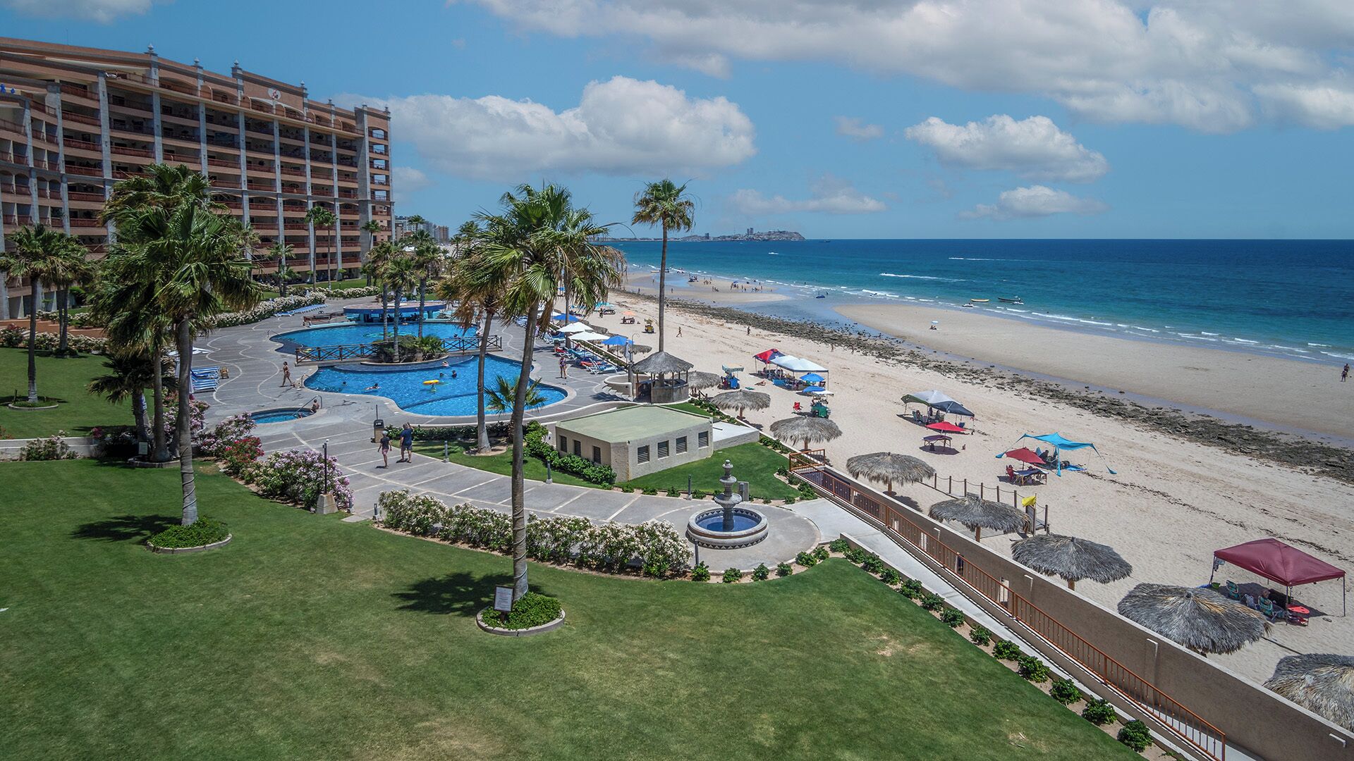 Un resort con un amplio espacio de piscina, acceso a la playa y vista al océano.