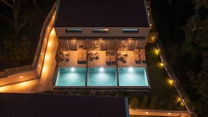 Un edificio moderno con área de piscina en la azotea, varias piscinas e iluminación exterior.