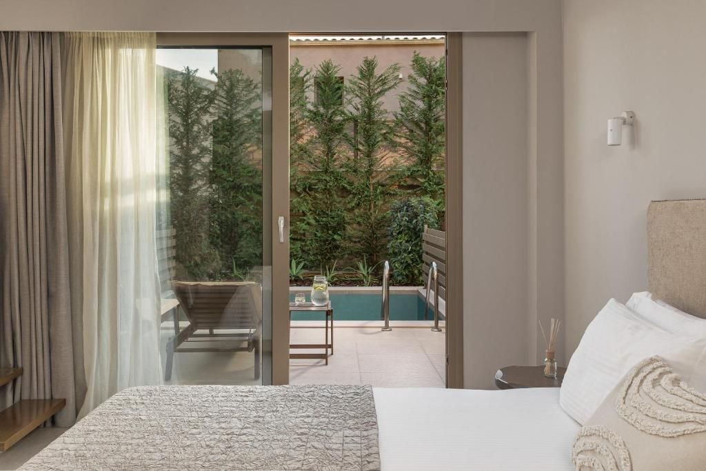 A hotel room with a bed, a sliding glass door leading to a pool area, and a view of trees.