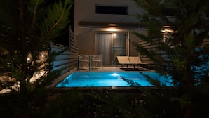 Un edificio moderno con piscina, dos sillones de descanso y puerta de acceso de vidrio.