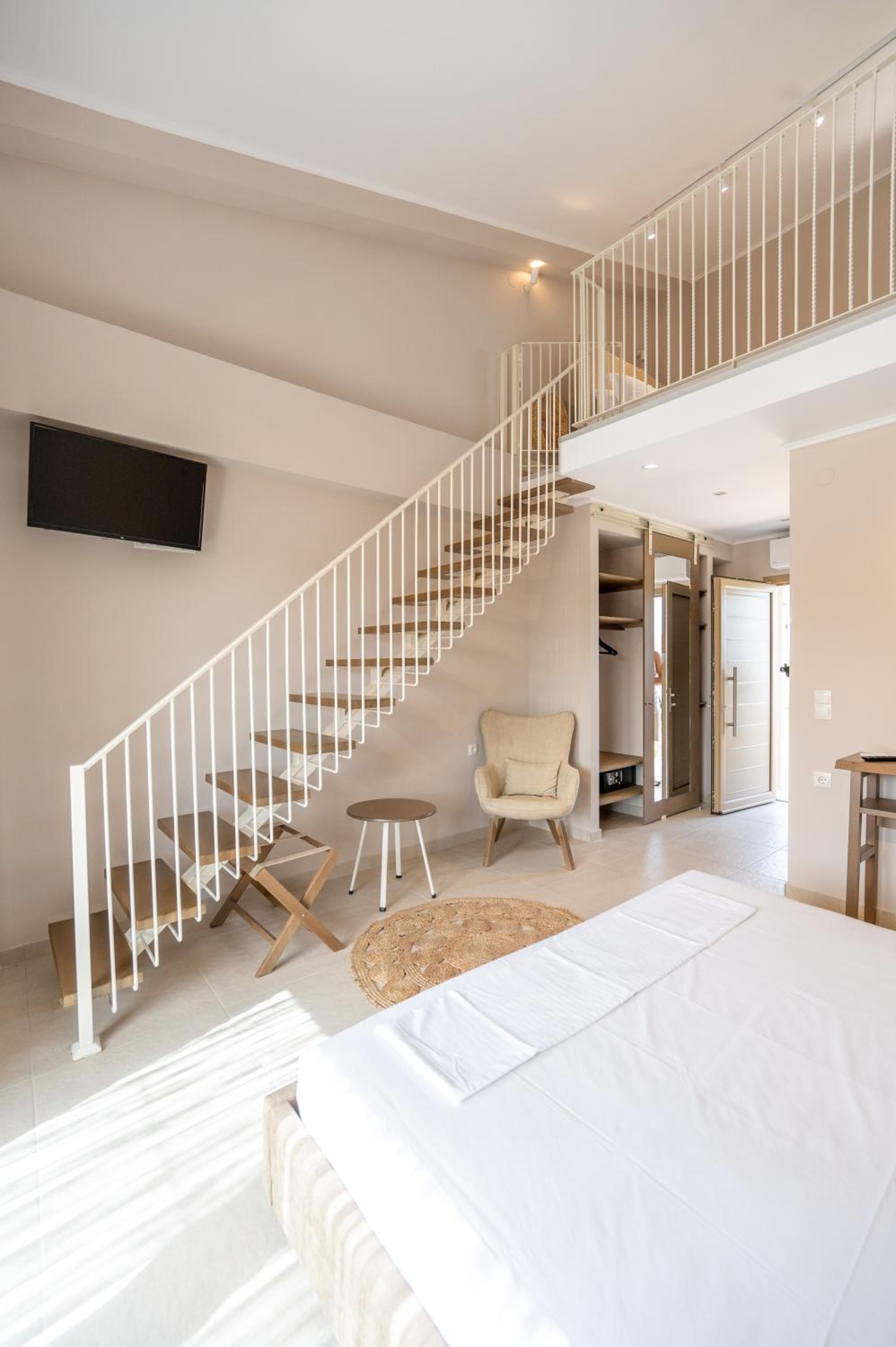 A spacious bedroom with a large bed, a chair, a small round table, and a staircase leading to an upper level.