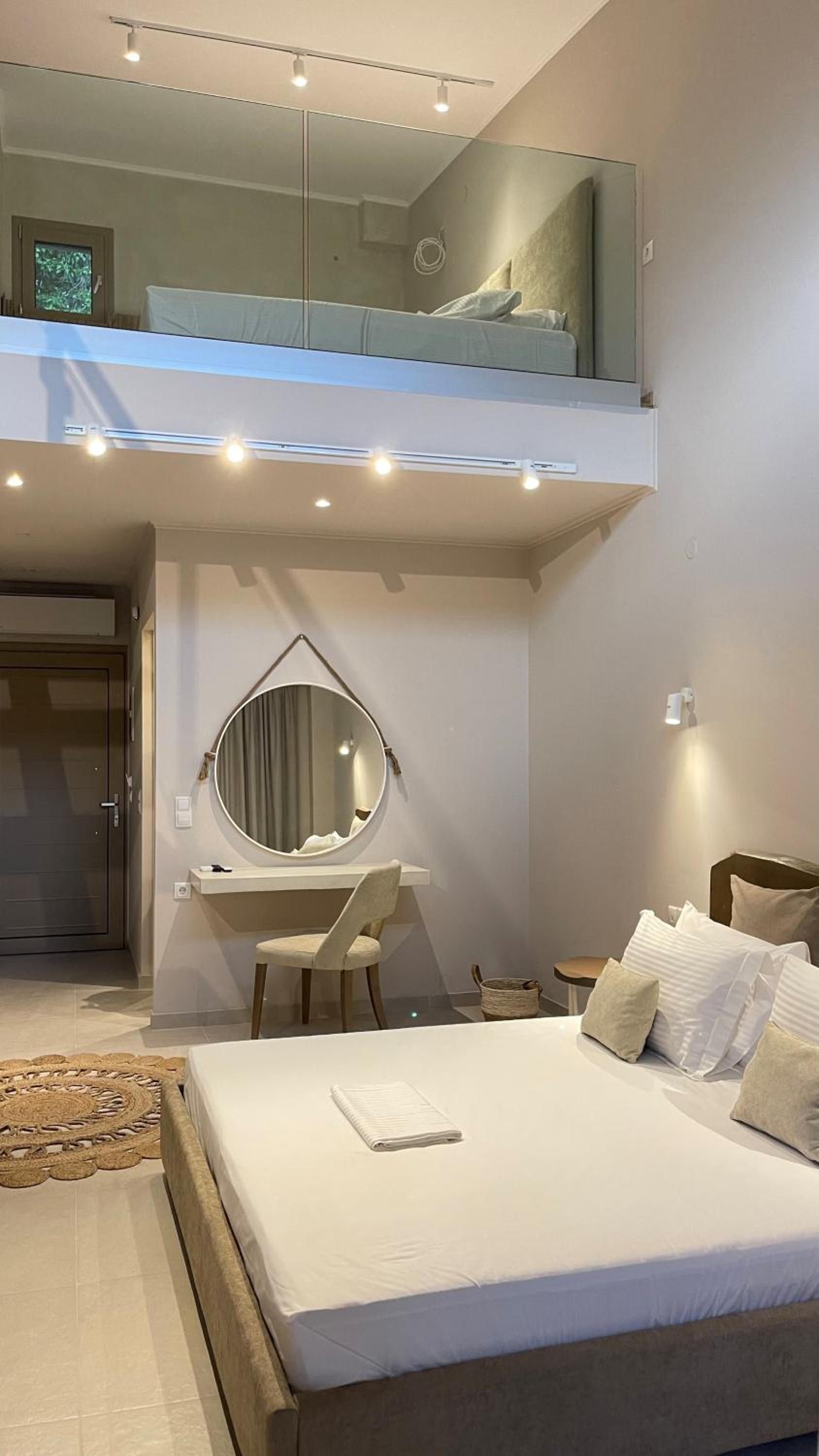 A modern bedroom with a bed, a desk, a chair, a round mirror, and a small balcony.