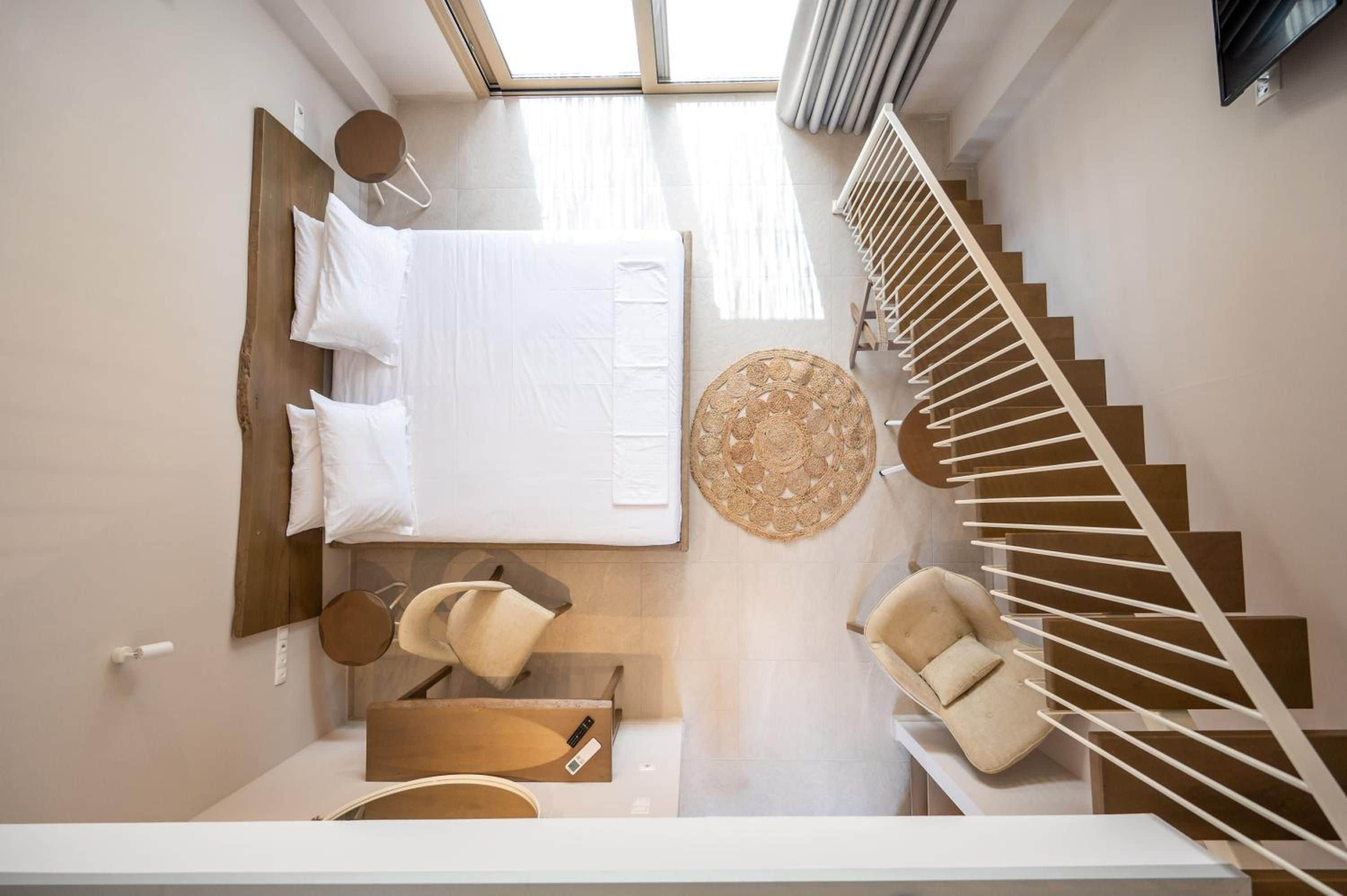 A modern bedroom with a large bed, a round woven rug, a chair, and a staircase.