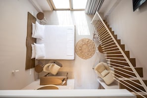 A modern bedroom with a large bed, a round woven rug, a chair, and a staircase. - Scarabeo Suites & Villas (Parga)