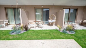 Un patio moderno al aire libre con una mecedora, una mesa de comedor con sillas y un pequeño jardín con plantas y una cerca decorativa.