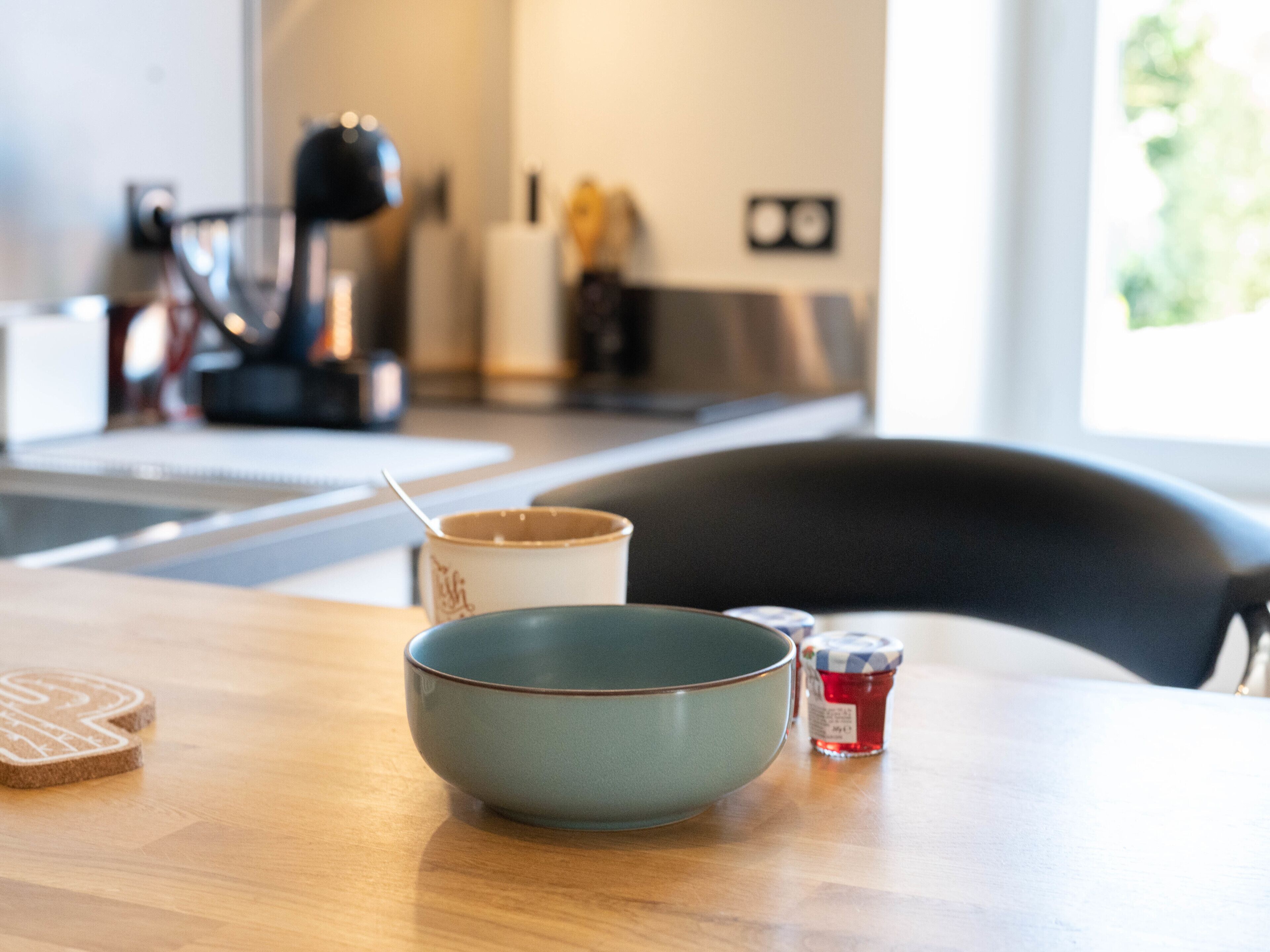 Une cuisine avec une table en bois, un bol, une tasse et un pot de confiture.