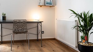 Habitación moderna con piso de madera, escritorio de metal, silla transparente, radiador y planta en maceta.