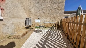 Un patio con pared de concreto, cerca de madera, una silla de metal, una mesa y un equipo de aire acondicionado.