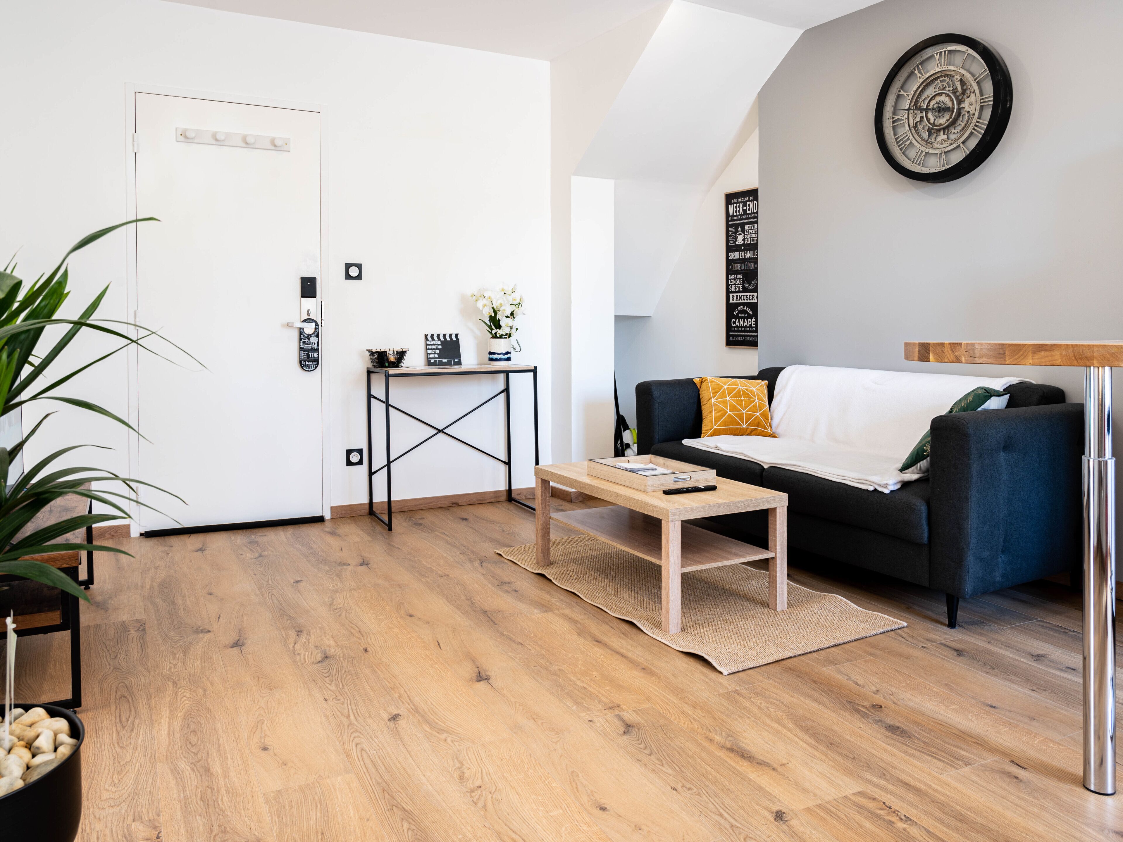 Un salon moderne avec un plancher en bois, un canapé bleu foncé, une table basse et une horloge murale.