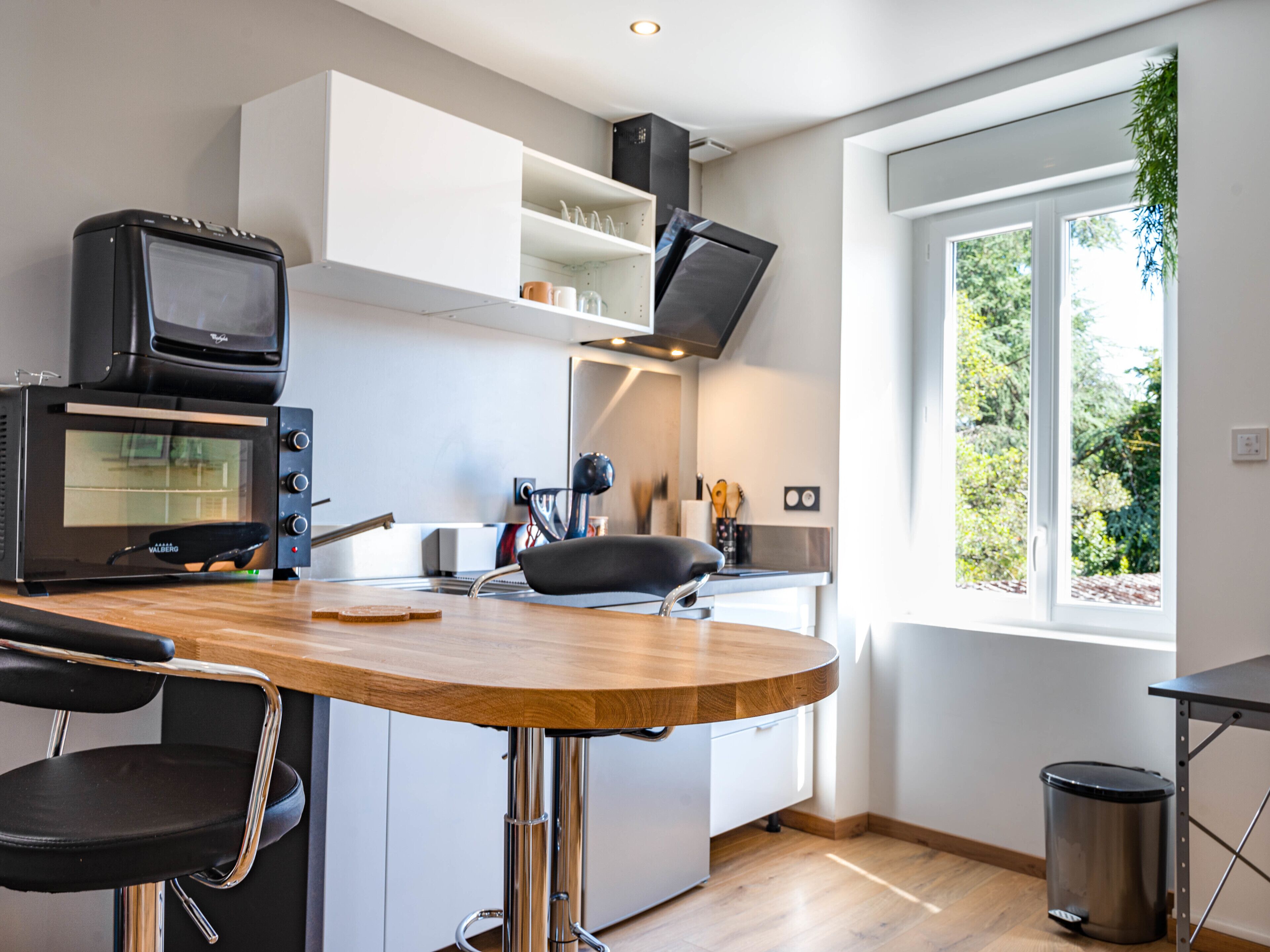 A modern kitchen with a built-in oven, a dining table with chairs, and a window providing a view of greenery outside.