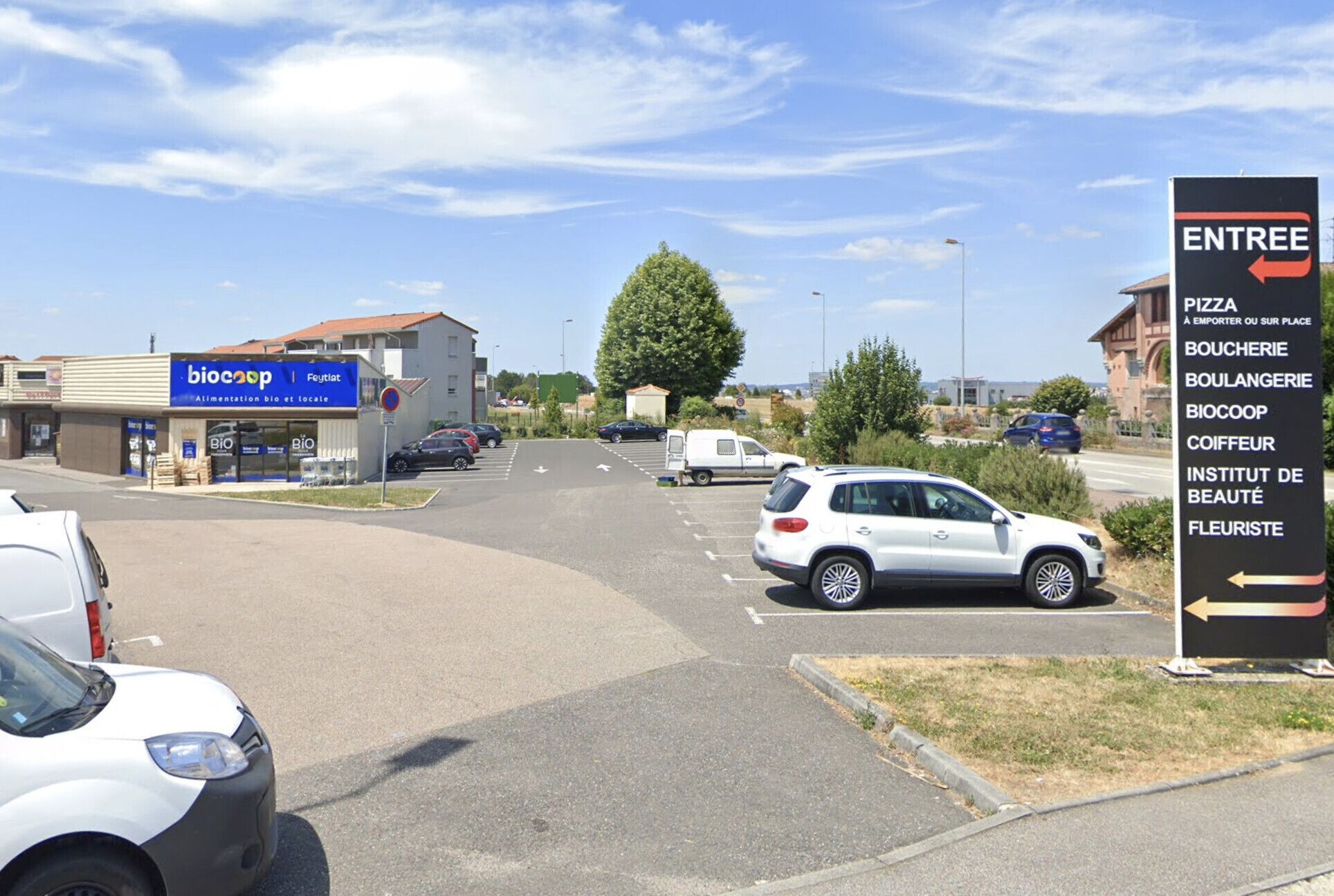 A parking lot with cars and a sign indicating directions to various local businesses.