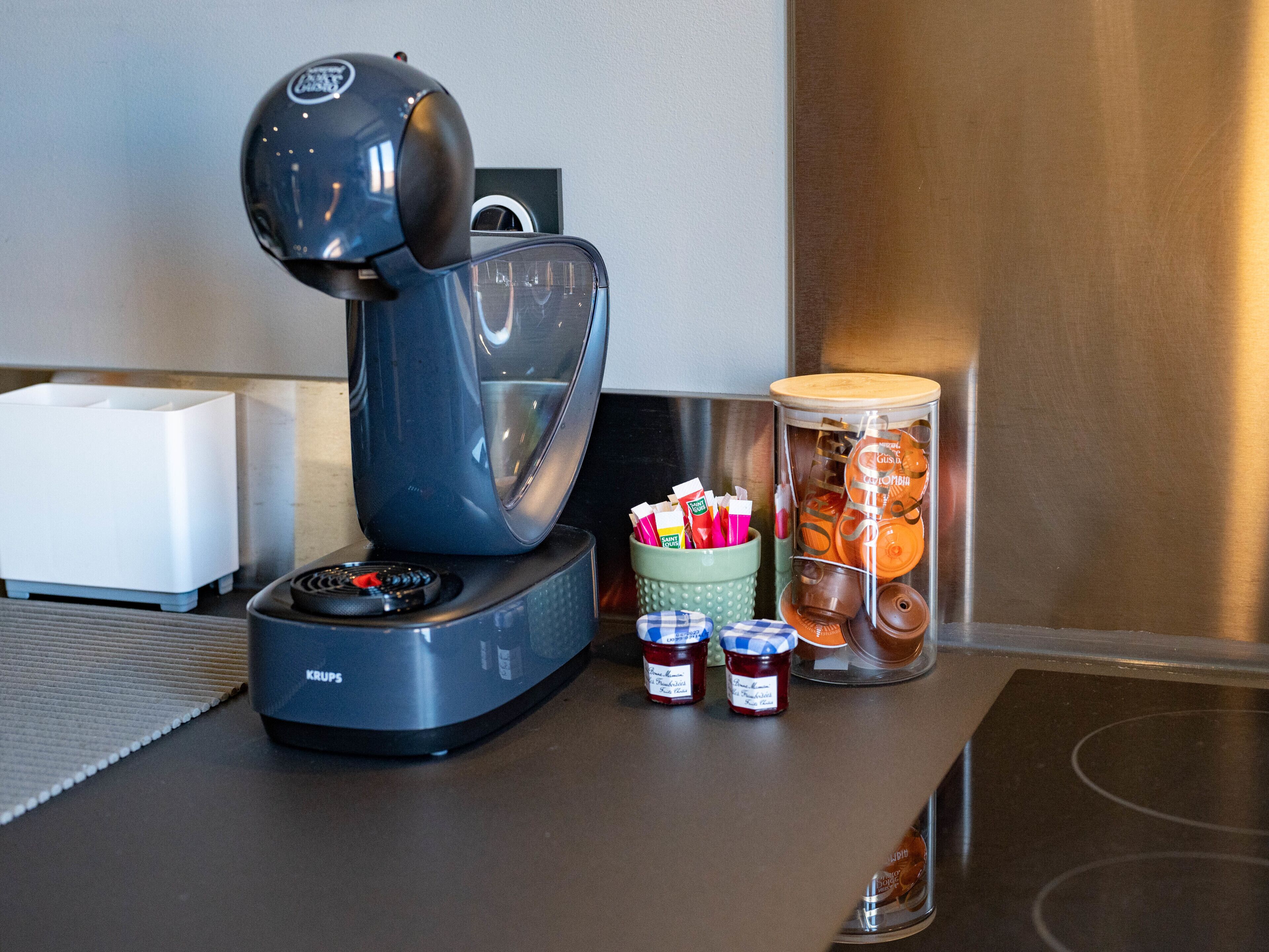 A coffee machine on a counter with a container of condiments and a jar of cookies.