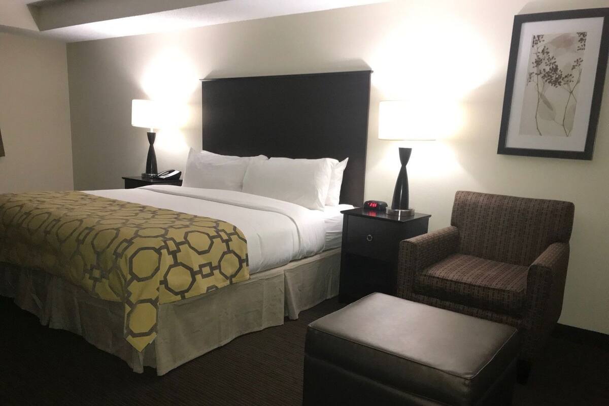 Ein Hotelzimmer mit Bett, Nachttischen, einem Sessel und einem gerahmten Bild an der Wand.
