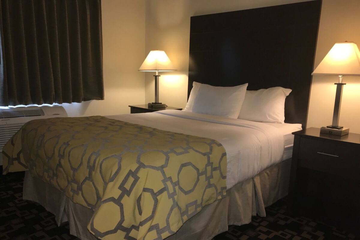 Ein Hotelzimmer mit einem Bett, zwei Nachttischlampen, einem Kopfteil, einem Nachttisch und einem gemusterten Teppich.