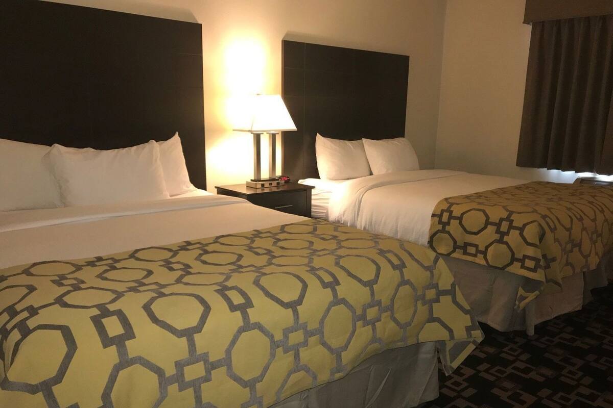Ein Hotelzimmer mit zwei Betten, einem Nachttisch mit Lampe und einem gemusterten Teppich.