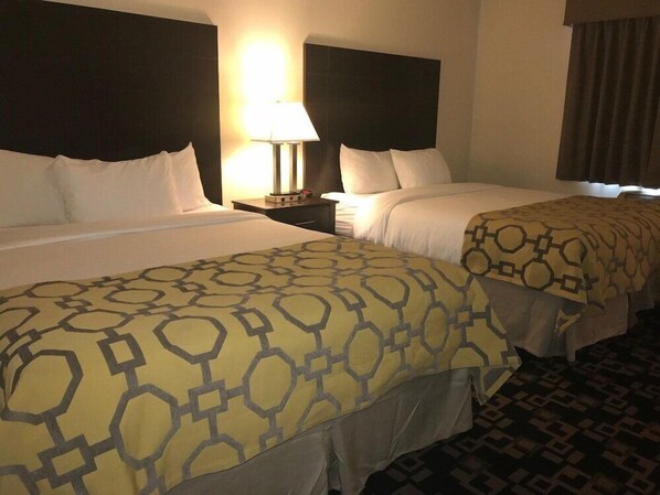 Una habitación de hotel con dos camas, una mesita de noche con lámpara y una alfombra estampada.