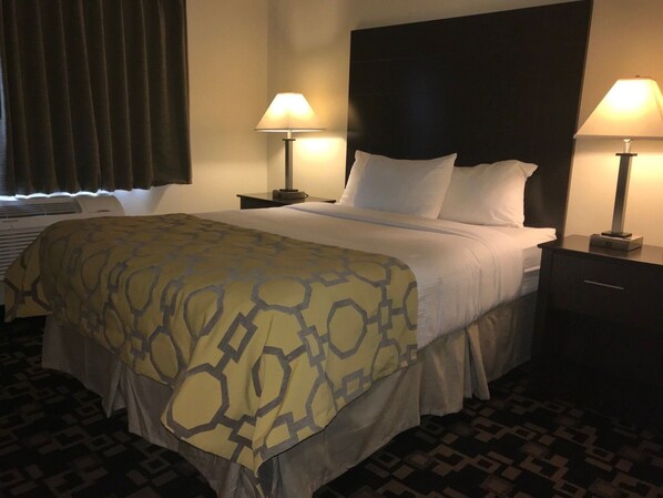 A hotel room with a large bed, two bedside lamps, a dark headboard, and a patterned bedspread. - Baymont By Wyndham Bloomington Msp Airport (Richfield)