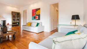 Un salon moderne avec un canapé blanc, une table basse en verre et un tableau abstrait aux couleurs vives accroché au mur.