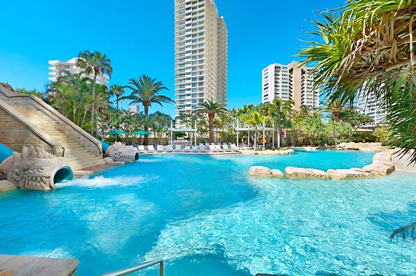 Relax by the pool surrounded by palm trees and modern architecture, featuring a unique waterfall and rock formations.