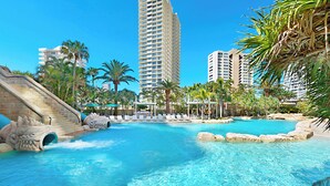 A swimming pool with a water slide, palm trees, and a view of tall buildings.