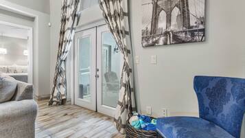 Un salon avec un canapé bleu à motifs, un canapé gris, un panier en osier contenant des vêtements pliés et une porte ornée de rideaux à motifs.