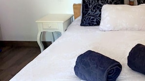 Camera da letto con testiera in legno, comodino bianco e letto con cuscini bianchi e blu scuro.