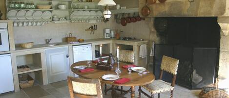 A traditional kitchen with a fireplace, wooden dining table, and chairs.