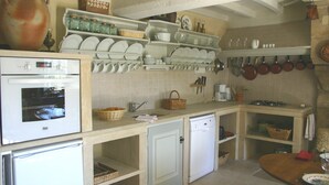 Cocina compacta con horno integrado, lavavajillas y pileta. Hay estantes sobre la encimera con platos y un colgador con ollas y sartenes.