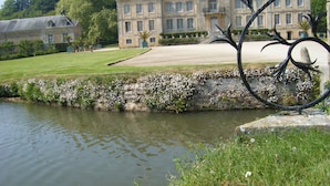 Un edificio grande y histórico con una fachada simétrica, un césped cuidado y una fuente de agua tranquila en primer plano.