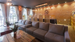 A cozy lounge area with a large sofa, wooden tables, and a brick wall. - Tran Vien Dong Hotel (Nha Trang)