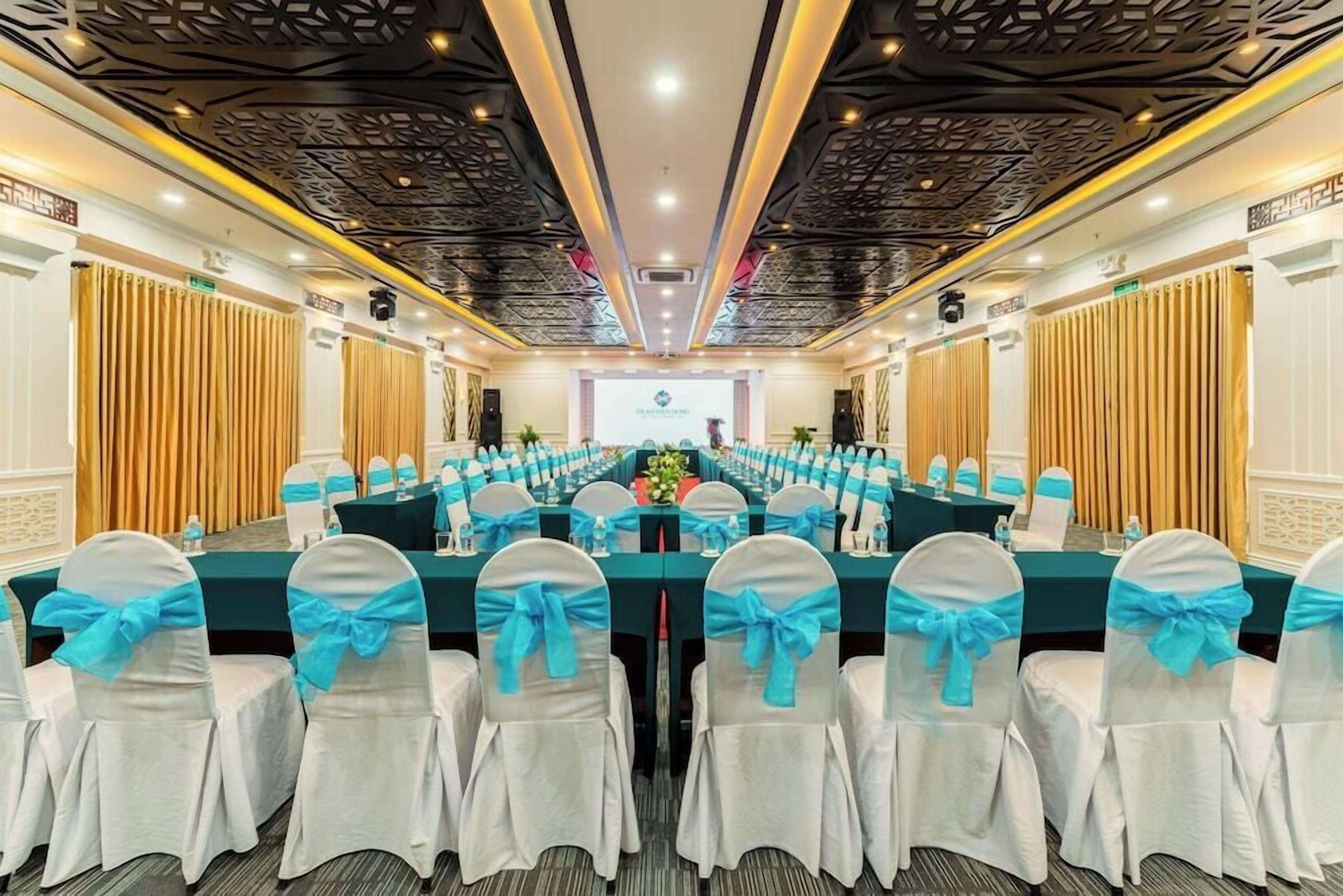 A conference room with a long table, white chairs with blue sashes, and a stage at the front.