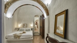 A bedroom with a bed, a vanity with a mirror, and a hallway leading to another room. - Villa Murat (Santorini)