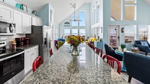 A spacious kitchen with granite countertops, white cabinets, and a central island with a vase of flowers. - Beachfront | Hot Tub, Bar & Stunning Views (Bolivar Peninsula)