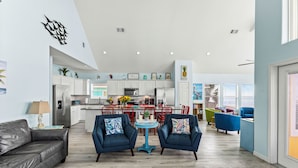 A modern living room with a grey sofa, two blue armchairs, and a small round table with a plant. - Beachfront | Hot Tub, Bar & Stunning Views (Bolivar Peninsula)