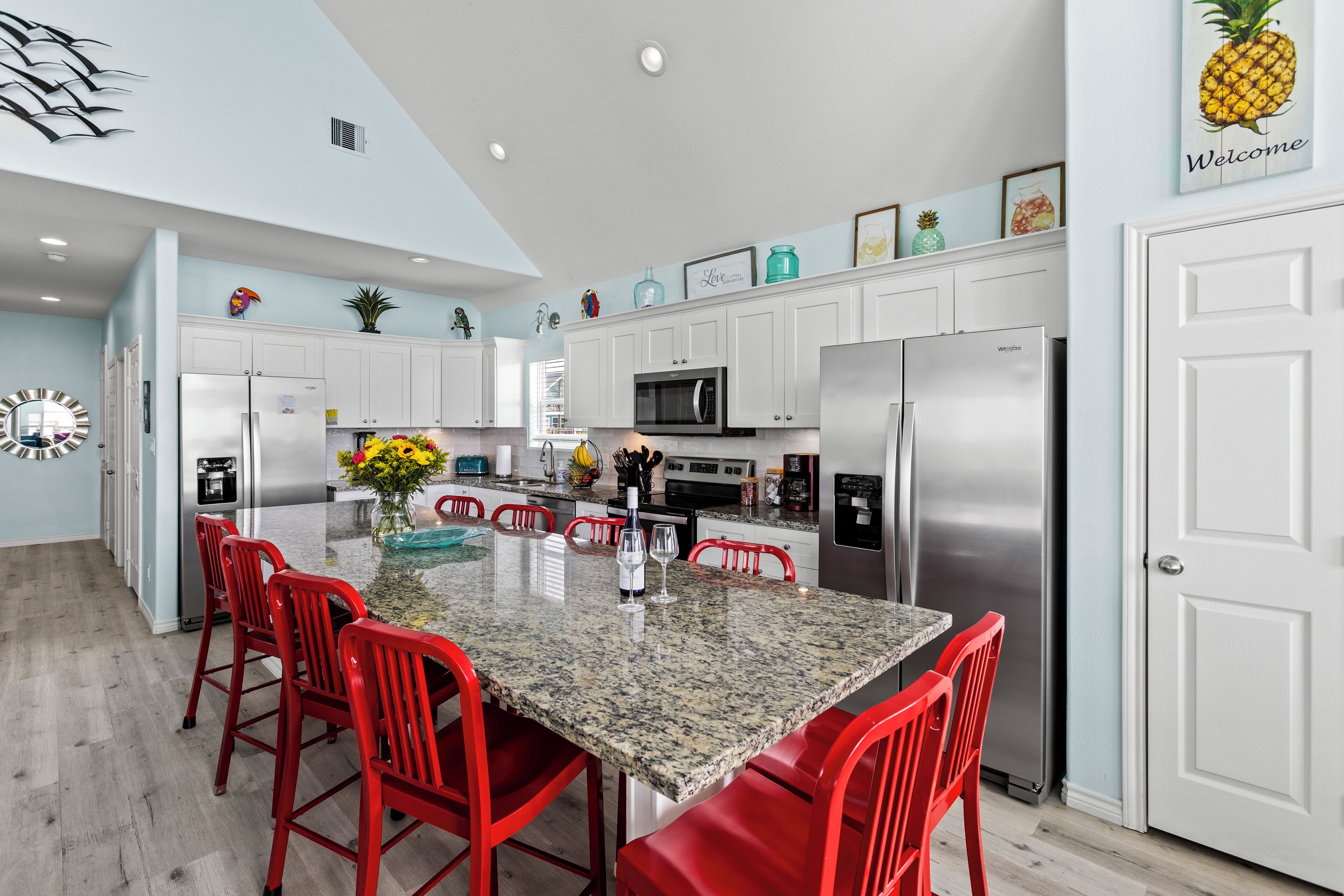 A modern kitchen with white cabinets, a granite island, red bar stools, and a stainless steel refrigerator.