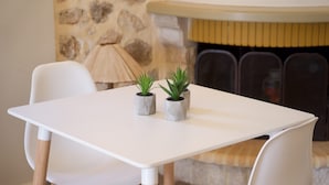 Taula blanca amb dues plantes en testos, caires blancs i una paret de pedra amb una llar de foc al fons.