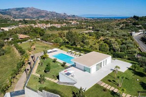Relax in a spacious outdoor area with a rectangular swimming pool and covered patio, surrounded by lush greenery and offering panoramic views of the surrounding landscape.