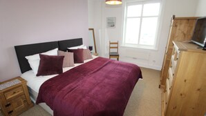 Une chambre à coucher avec un grand lit, une commode en bois, une chaise et un téléviseur.
