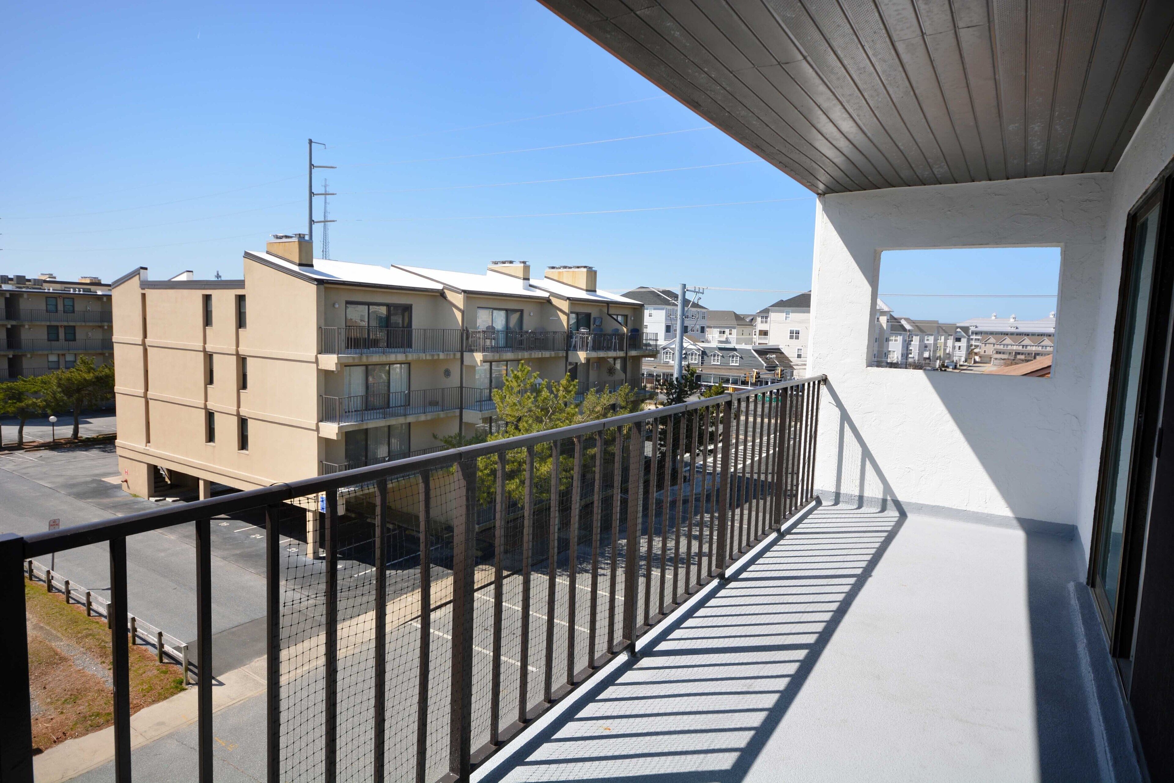 A balcony with a metal railing overlooking a parking lot and residential buildings.