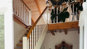 Eine Holztreppe mit weißen Geländern führt zu einer zweiten Etage, ein Holzschrank mit Glastüren und ein gemustertes Teppich im Raum.