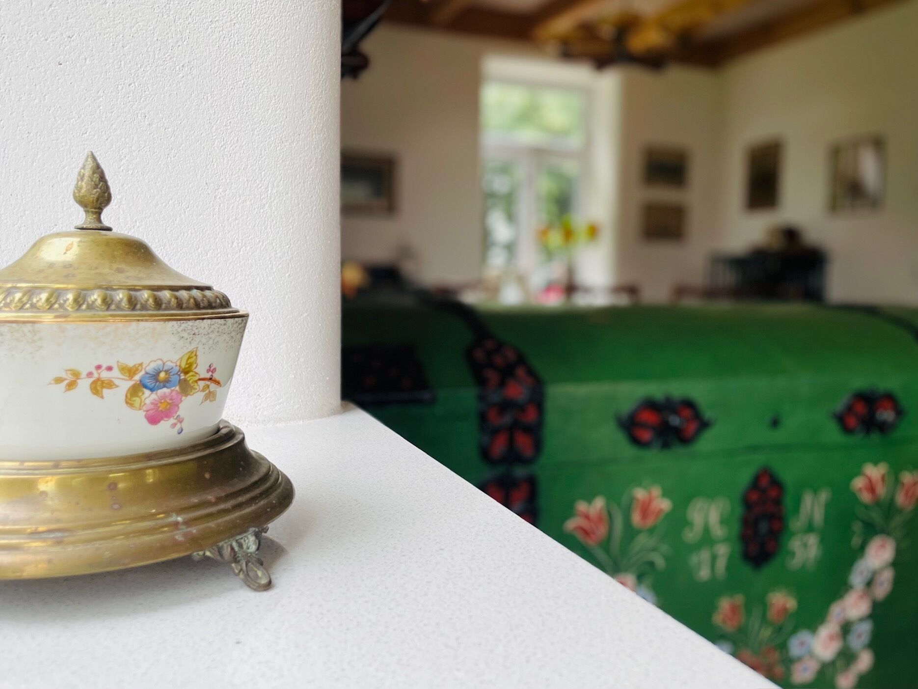 A room with a white column, a green bed with floral patterns, and a decorative brass object.
