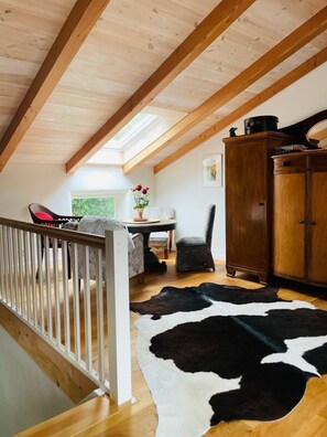 Een loft-achtige kamer met een houten plafond, een vachttapijt, een eettafel met stoelen en een houten kast.