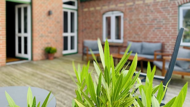 Ein Backsteinhaus mit einer Holzdachterrasse, Sitzgelegenheiten im Freien und einem Blumentopf.
