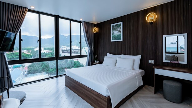 A modern hotel room with a large bed, a desk, and a view of the cityscape through large windows. - Tuan Ninh Hotel 2  (Ho Chi Minh City)