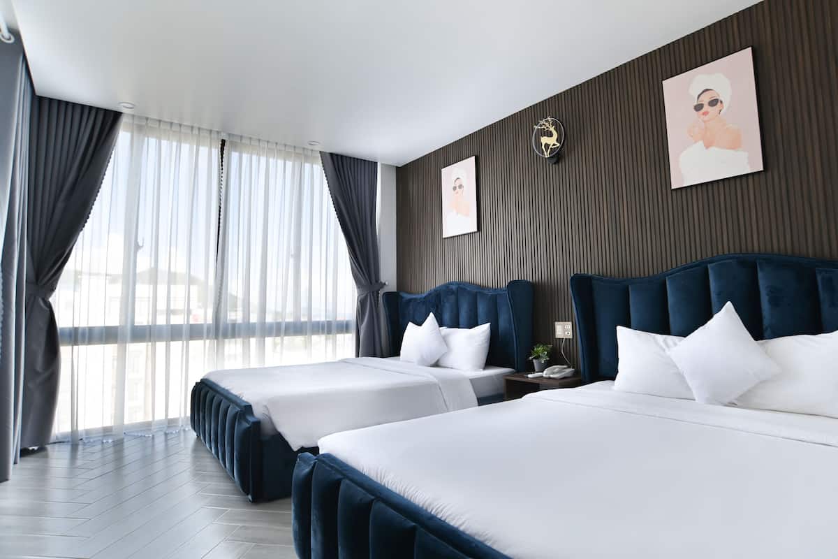 Habitación de hotel con dos camas, un ventanal con cortinas, un reloj en la pared y un cuadro enmarcado.