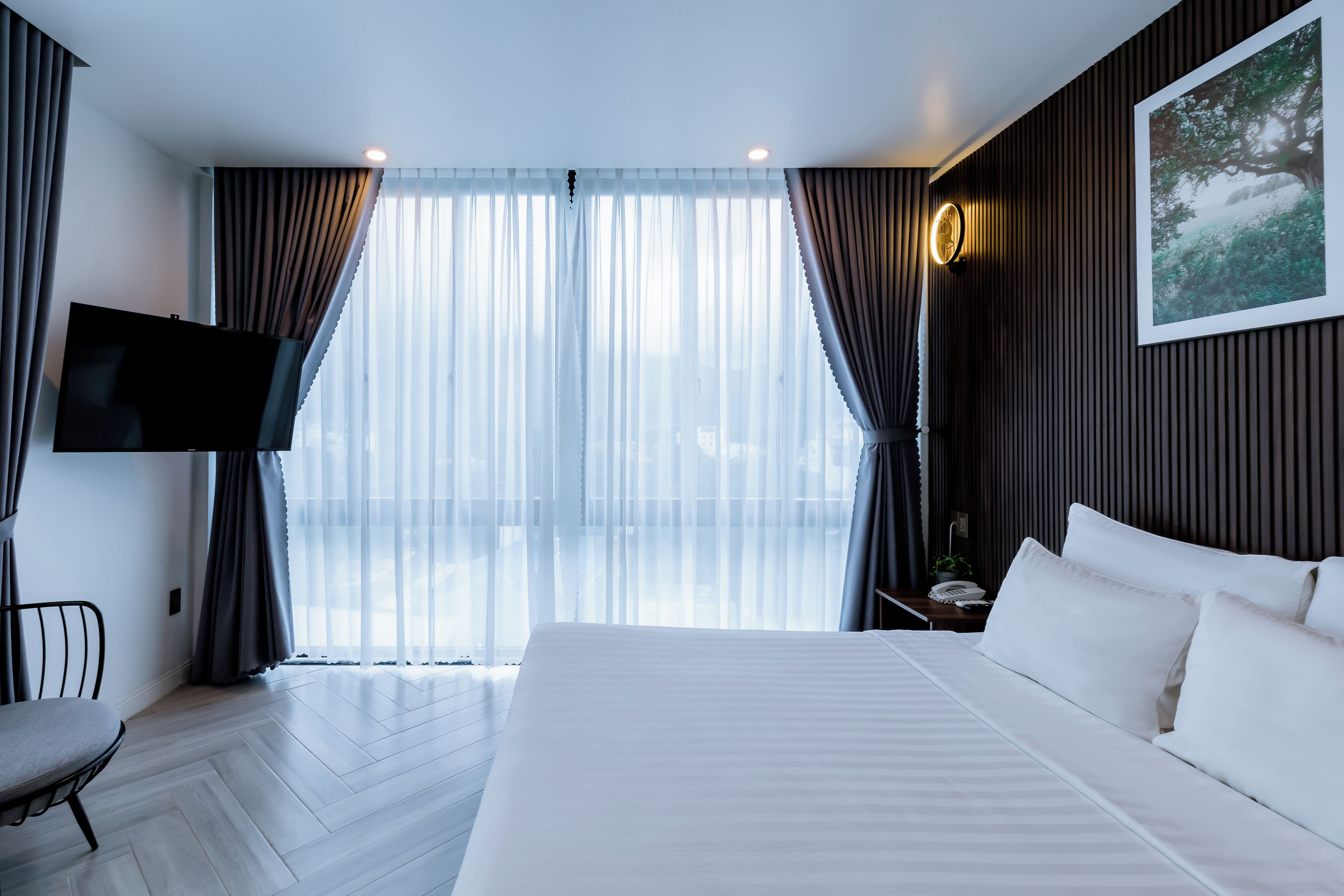 Une chambre d’hôtel avec un grand lit, une télévision, un fauteuil et une vue sur l’extérieur à travers des rideaux transparents.