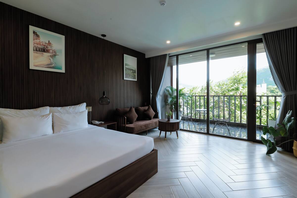 Una habitación de hotel moderna con una cama grande, un sofá, una mesita y un balcón con vistas.