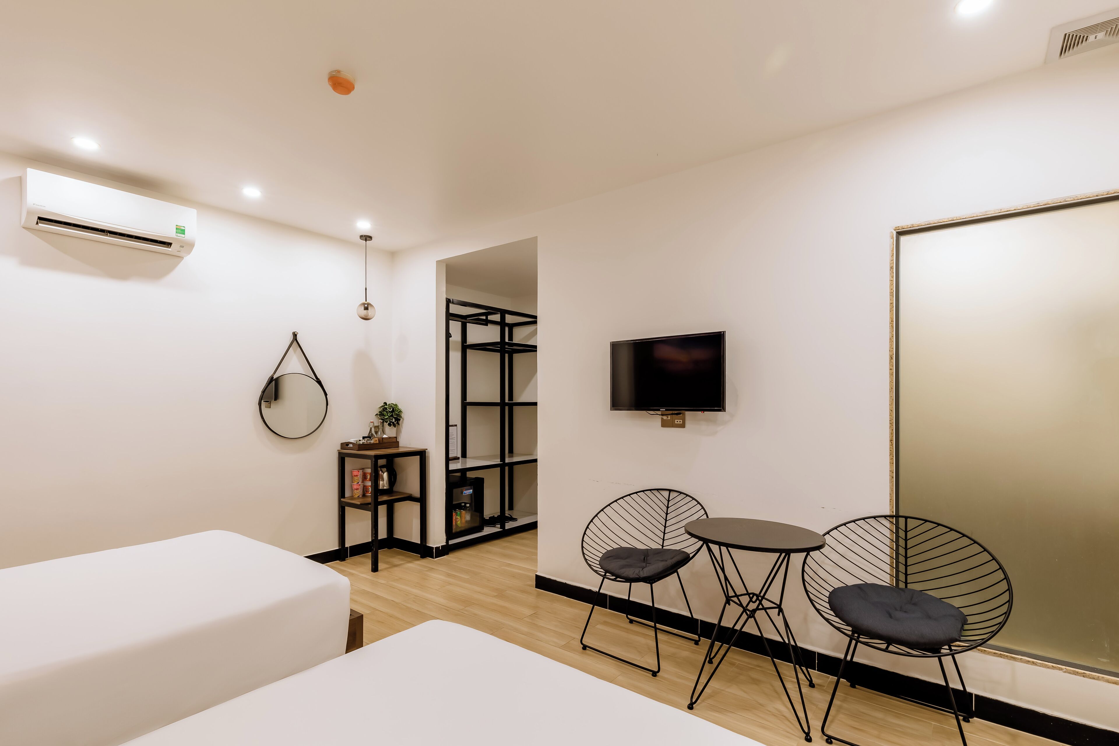 Una habitación de hotel moderna con una cama, una mesita pequeña con dos sillas, un televisor y un espejo grande.