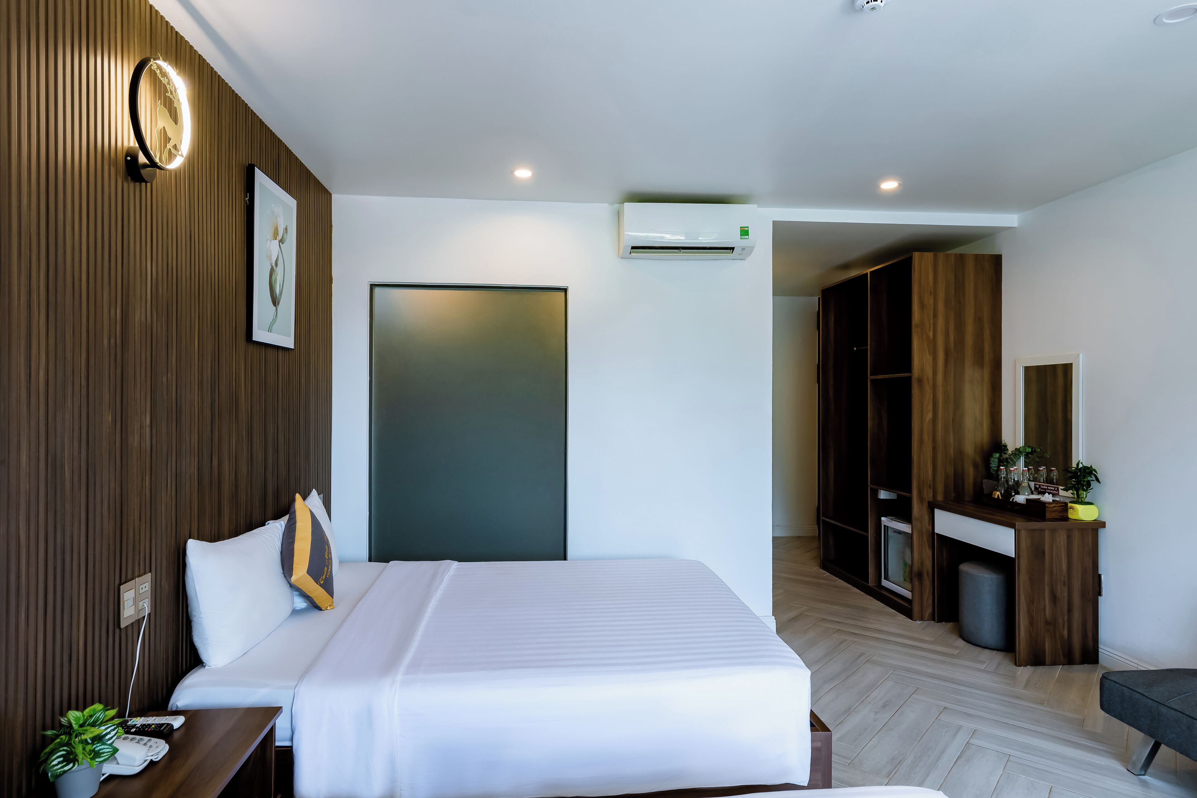 Una habitación de hotel moderna con una cama grande, un escritorio con computadora, un armario y un equipo de aire acondicionado.